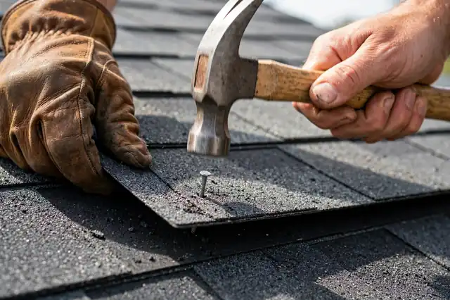 Roofer hammering a nail into an asphalt shingle during repair